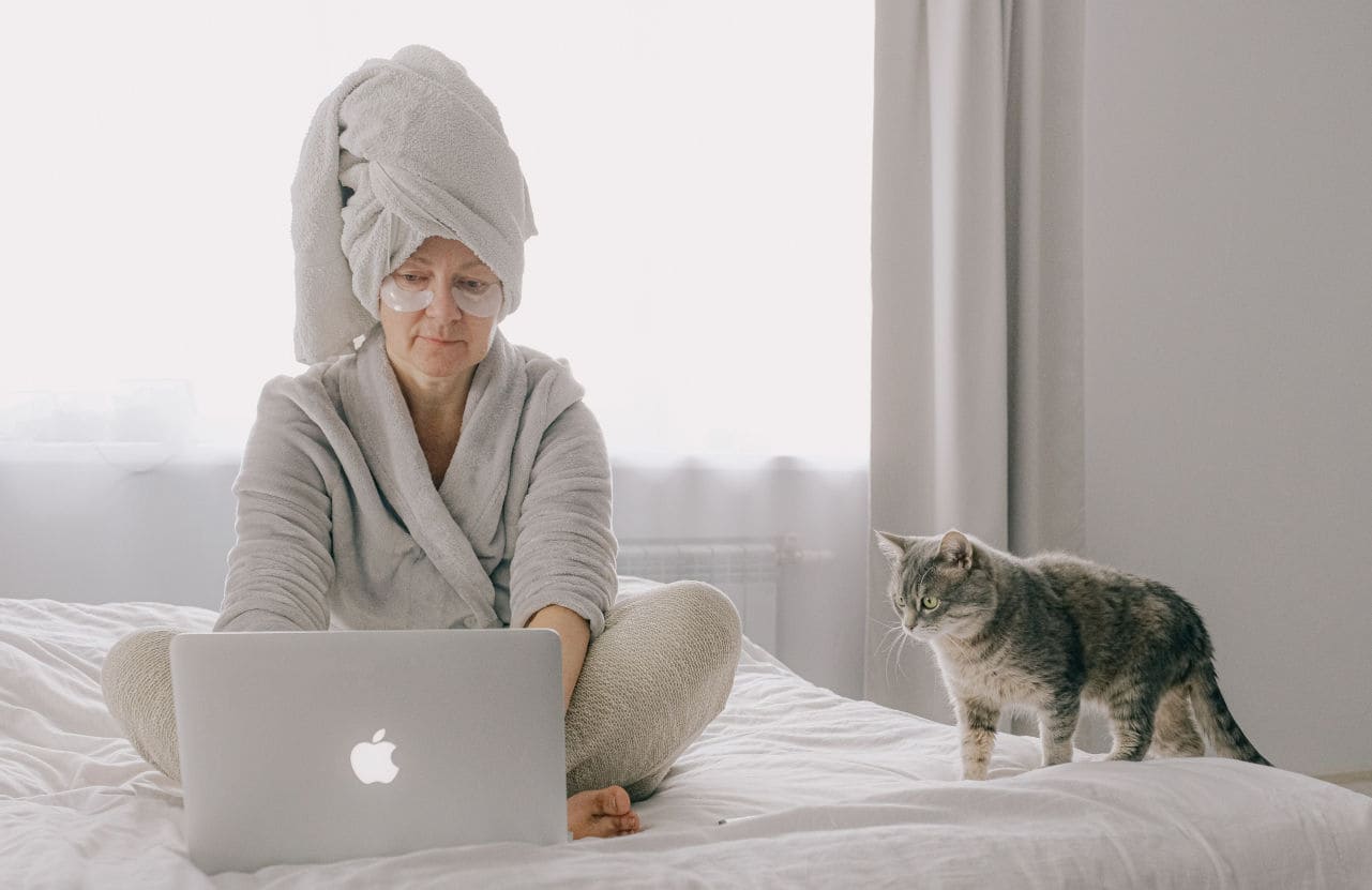 femme avec serviette sur la tête, assise sur son lit, regarde ordinateur portable avec son chat
